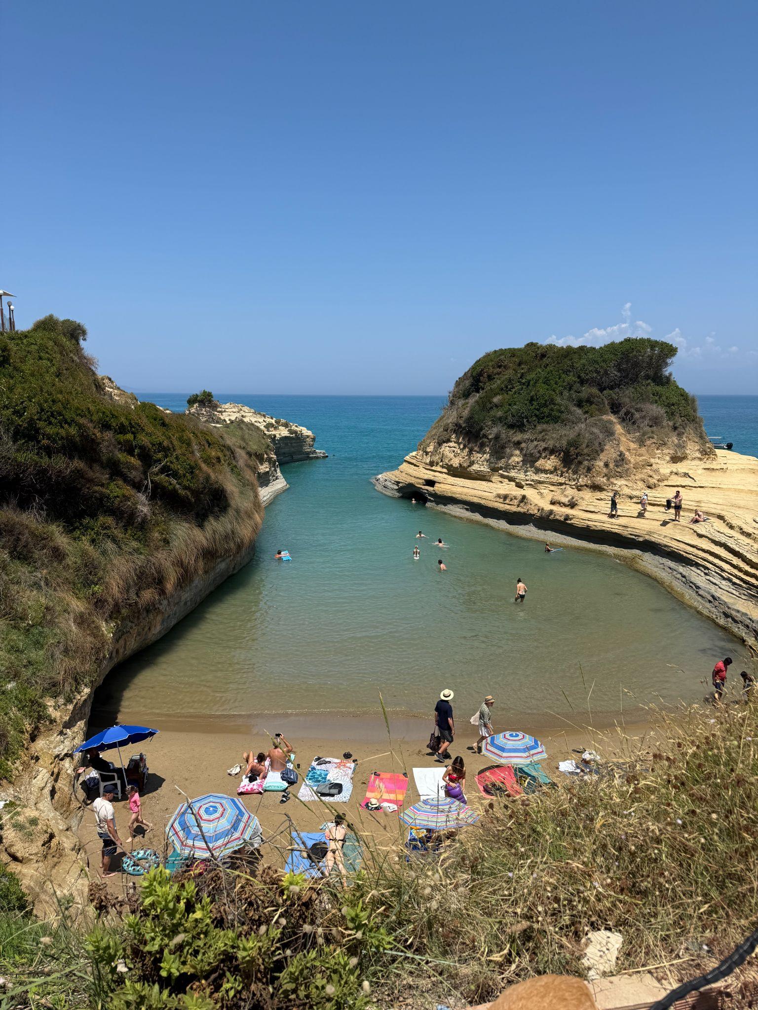 Swimmers and sunbathers at Canal d'Amour in Corfu, with turquoise water flowing between rocky cliffs