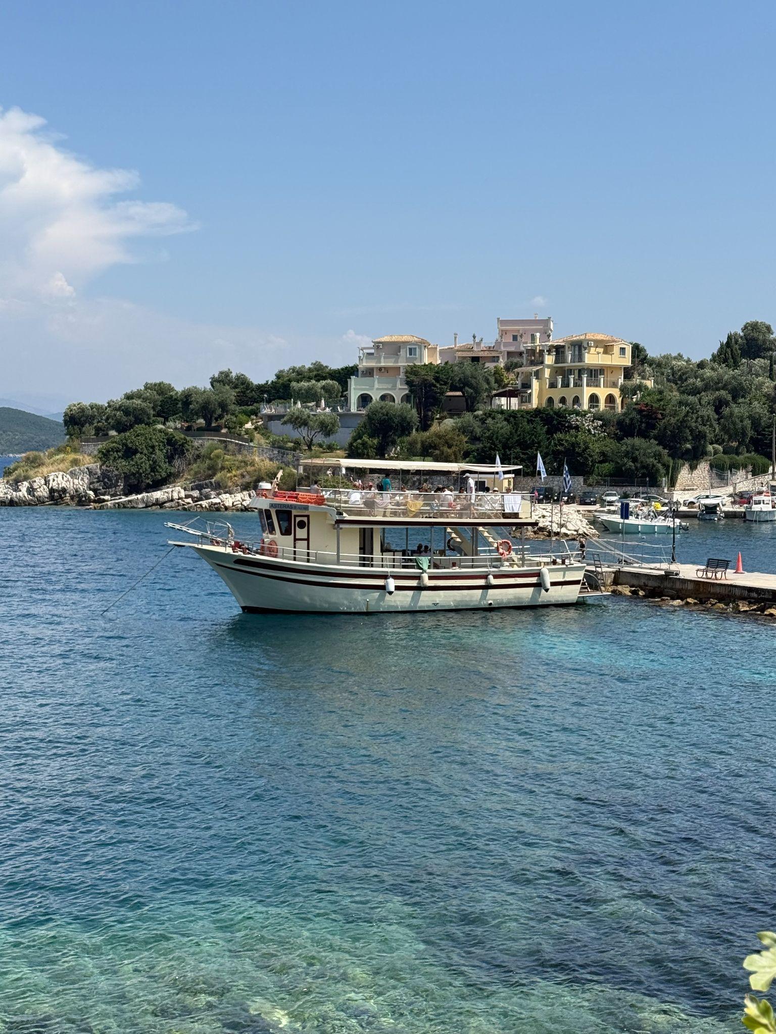 Traditional boat docked in the clear waters of Kassiopi harbor with hillside villas in the background