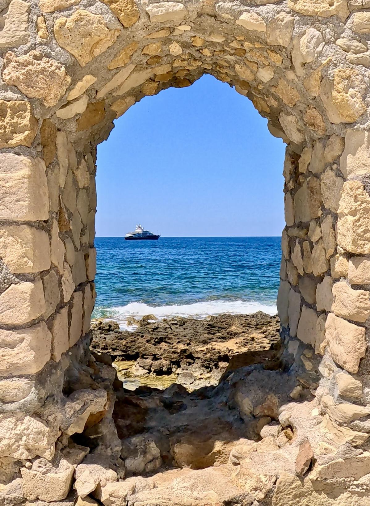 View of the sea and a yacht through a stone archway in Heraklion, Crete
