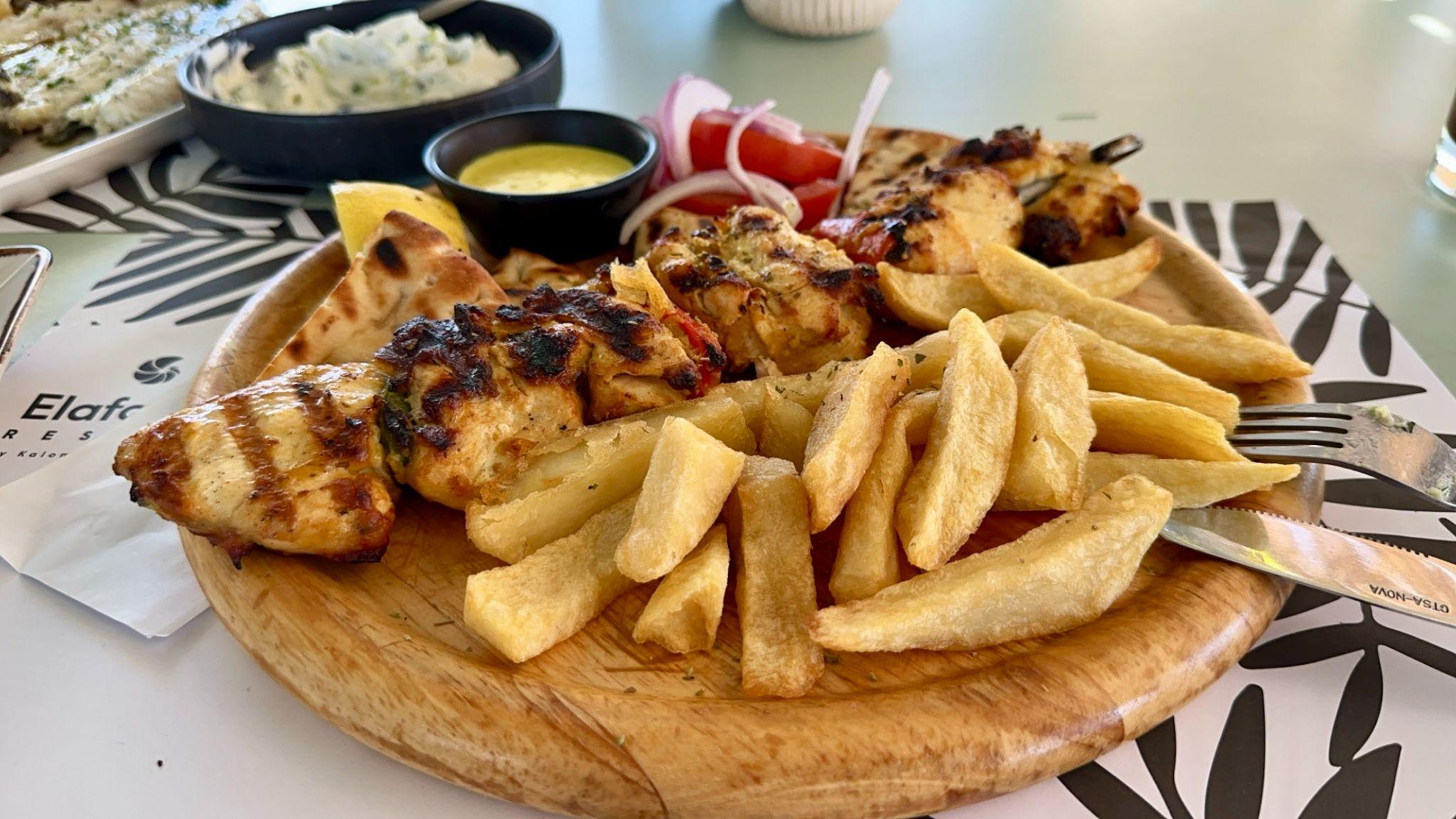 Chicken souvlaki with fries and dipping sauces served on a wooden board near Elafonissi Beach, Crete