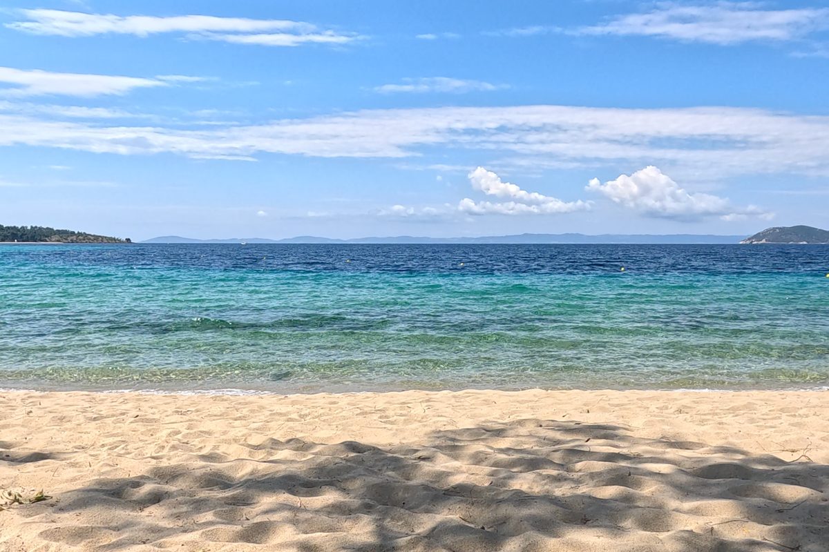 Sandy beach with sun loungers and clear turquoise water at a beach club in Halkidiki