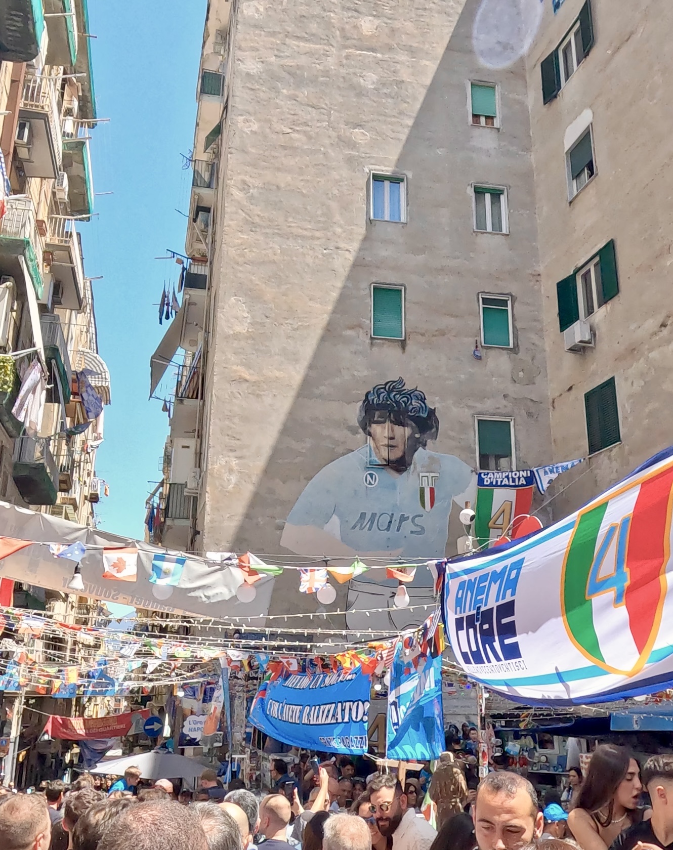 Maradona mural on a building wall in the Spanish Quarters of Naples with fans celebrating below