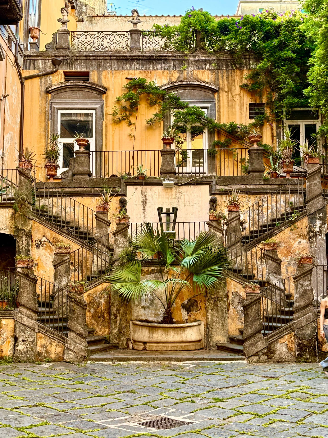 Ornate staircase with potted plants and iron railings in a historic Naples courtyard
